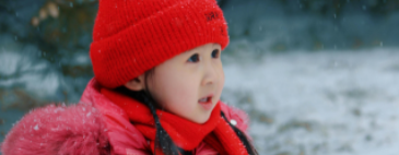 little girl in red hat and red winter coat sitting in the snow