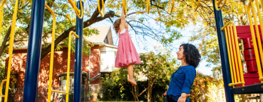 Mother and daugher playing on a playground together (Mother watching daughter swinging on monkey bars)