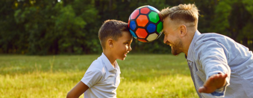 Photo of boy and dad facing one another with a soccer ball being held between their foreheads